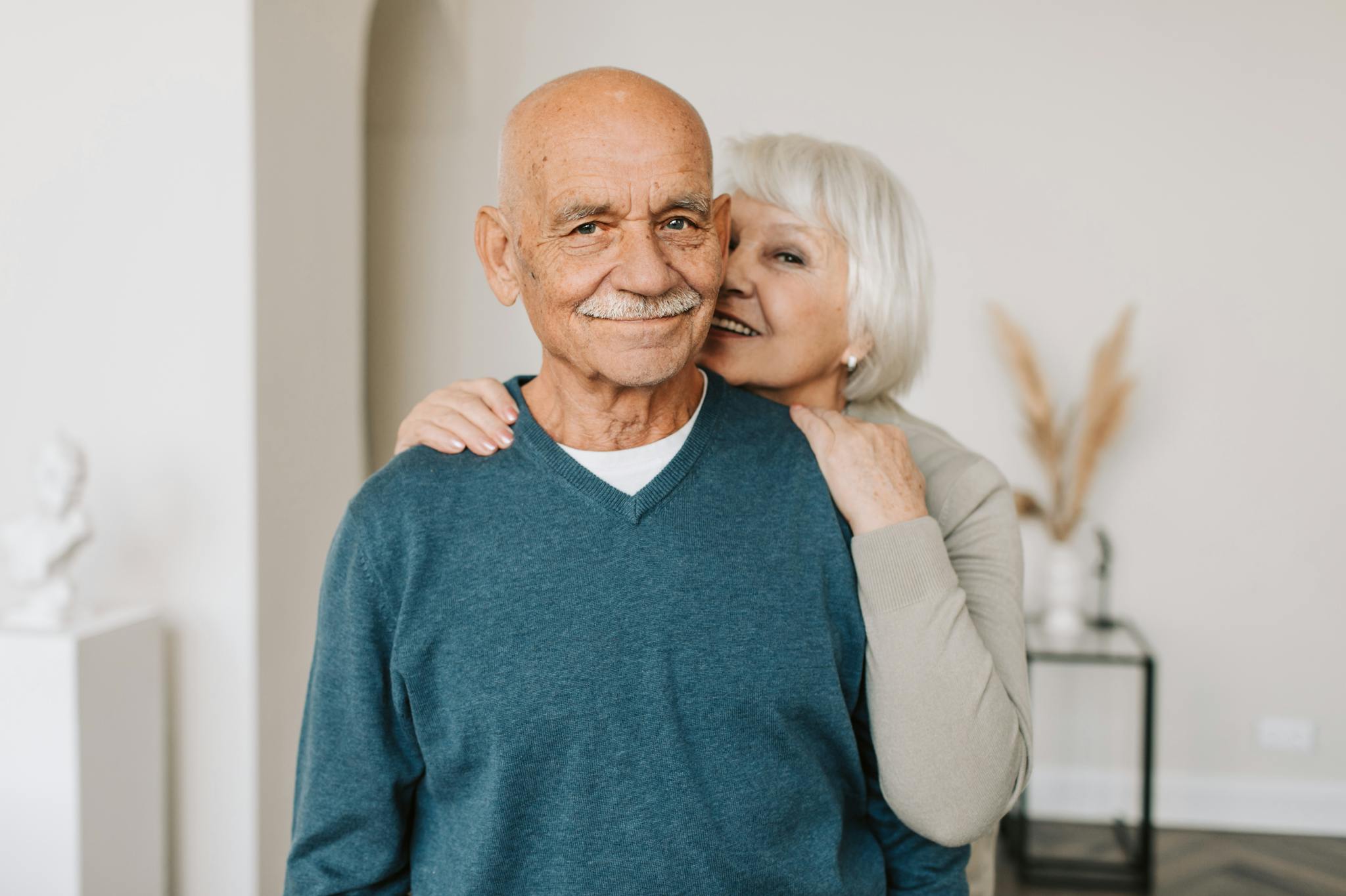 A joyful elderly couple embracing each other in a cozy indoor setting, exuding love and happiness.